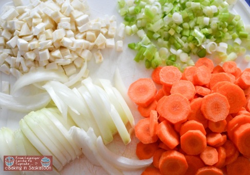 Chopped celery root, green onions, carrots, and sliced onions on a cutting board. 